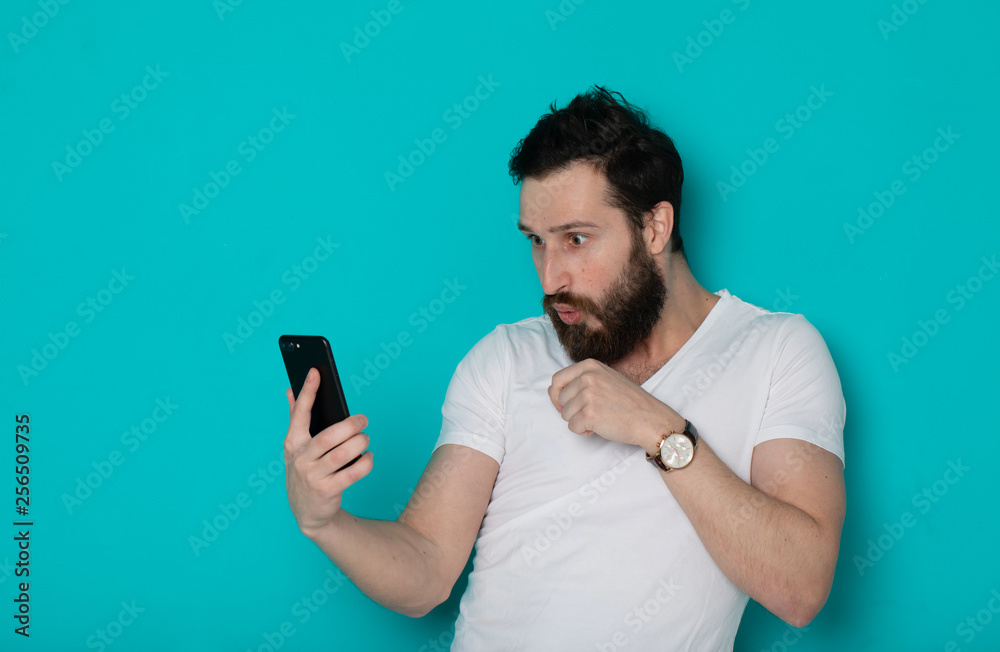 Portrait of a surprised casual man looking at mobile phone isolated over blue background Portrait of a surprised casual man looking at mobile phone isolated over blue background