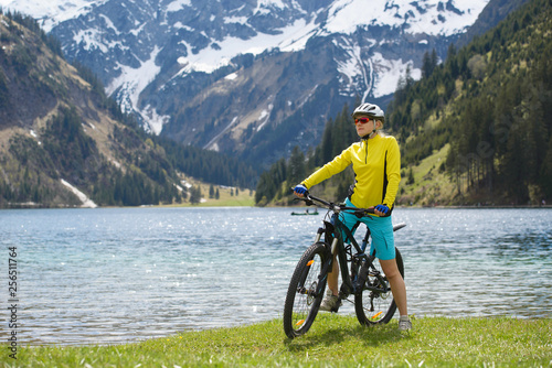 Young woman riding a bike on the lake in a beautiful mountain landscape