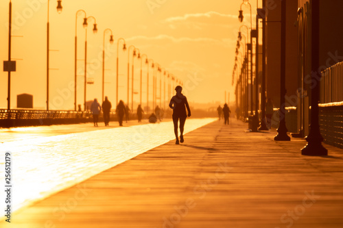 Silhouette of a person running on a boardwalk at sunset. People enjoying outdoor activities under golden light - Long Beach New York