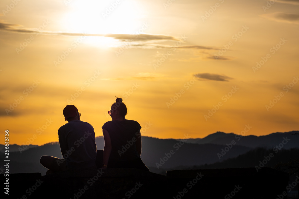 Teenager couple with sunglasses sitting on hill enjoying the sunset