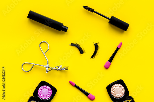 decorative cosmetic set with lash curler and mascara on yellow woman desk background top view