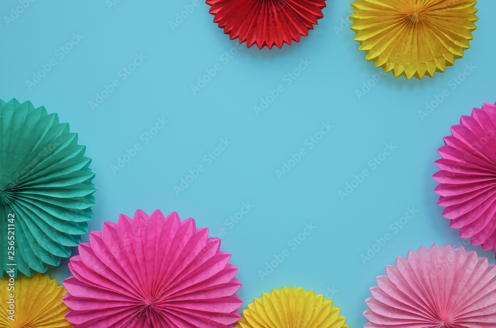Color paper flowers on blue background. Festive or party background. Flat lay style. Copy space for text. Birthday greeting card.