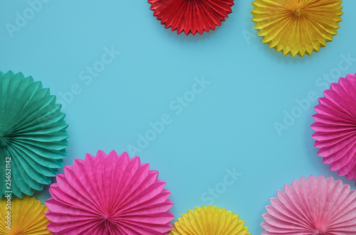 Color paper flowers on blue background. Festive or party background. Flat lay style. Copy space for text. Birthday greeting card.