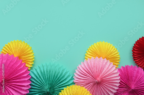 Different paper flowers on green table top view. Festive or party background. Flat lay style. Copy space for text. Birthday greeting card.