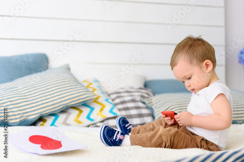 baby boy sitting on bed and playing on smartphone