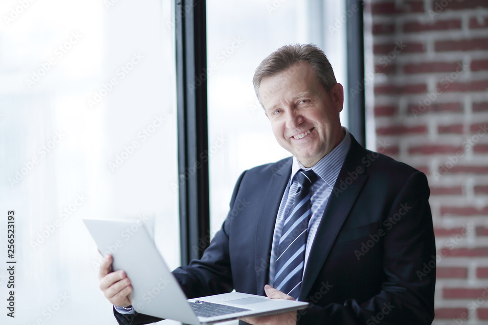 confident businessman with laptop standing in office.