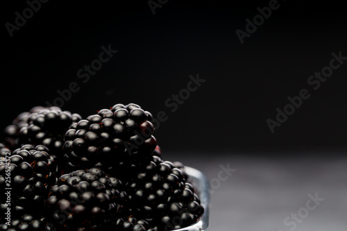 Photo of blackberry in plastic container on empty black background.