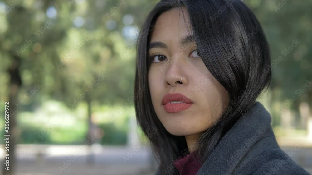 Attractive asian woman looking around in the park and staring at camera Attractive asian woman looking around in the park and staring at camera