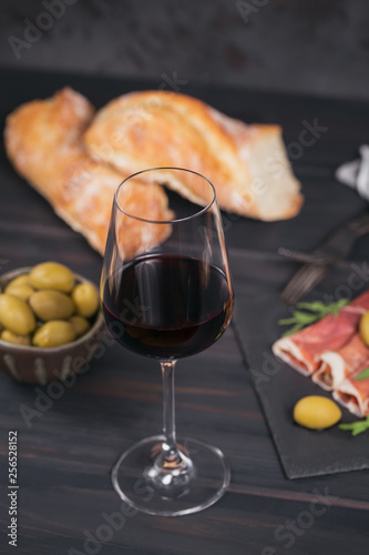 Glass of red wine with slices of cured ham or Spanish jamon serrano or Italian prosciutto crudo, bread, green olives and arugula
