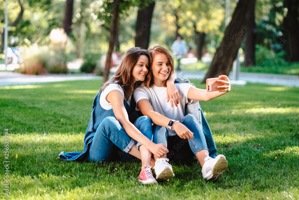 Fototapeta premium Two female friend sitting in the park have a rest take a selfie