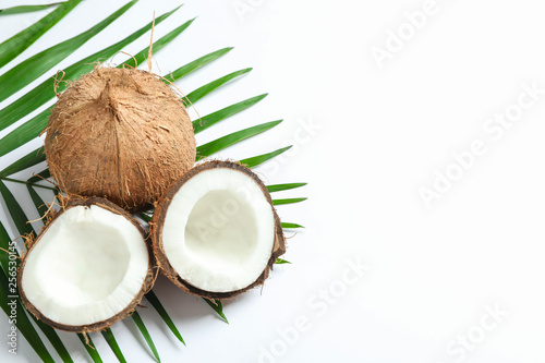 Two coconut one of which split with palm branch on white background