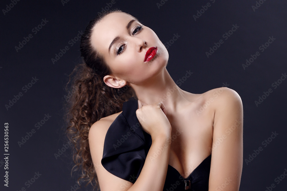 Portrait of beautiful young girl in a silk black dress with lace corsage on dark background. Elegant woman in a black dress on a dark background Portrait of beautiful young girl in a silk black dress with lace corsage on dark background. Elegant woman in a black dress on a dark background