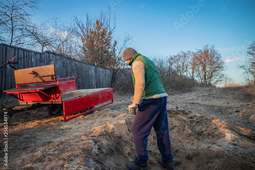 Man loads sand with a shovel into the trailer of the motoblock photo