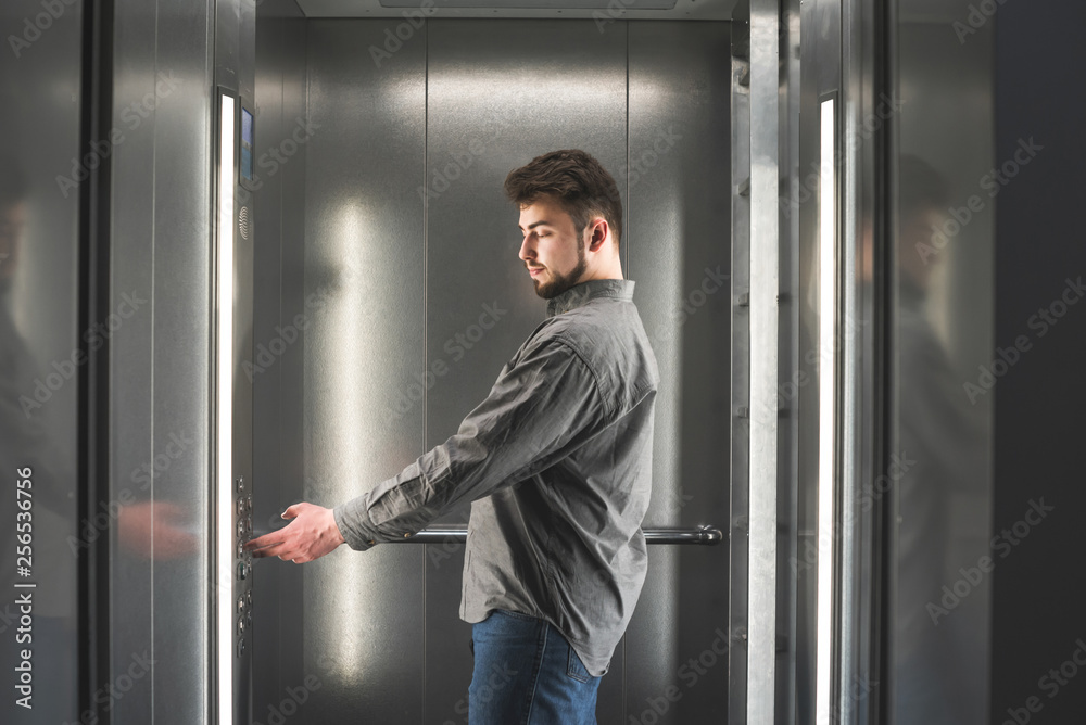 Business man with a beard and a shirt stands in the elevator and presses the floor button. Man worker pressing the button in the elevator. Business man with a beard and a shirt stands in the elevator and presses the floor button. Man worker pressing the button in the elevator.