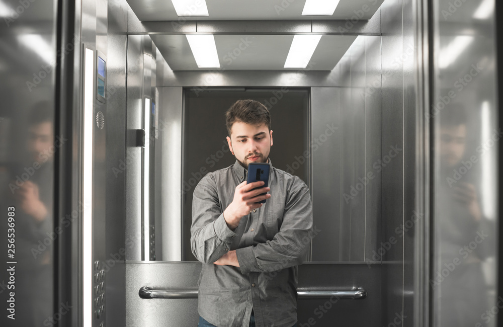 Busy man employee is watching on her smartphone screen in the lift. Shot of the businessman in the elevator using her smartphone. Busy man employee is watching on her smartphone screen in the lift. Shot of the businessman in the elevator using her smartphone.