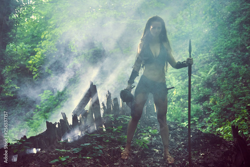 Beautiful amazon girl in metal mail with a spear in a misty forest.