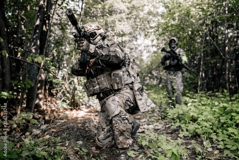 Armed soldiers in camouflage with sniper rifles walking along the path shoot at enemies