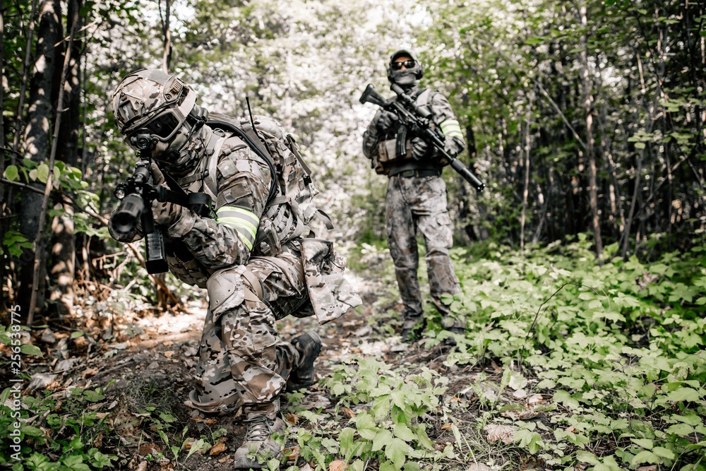 Armed soldiers in camouflage with sniper rifles walking along the path in the dense forest preparing for the assault. Military concept of disguised military