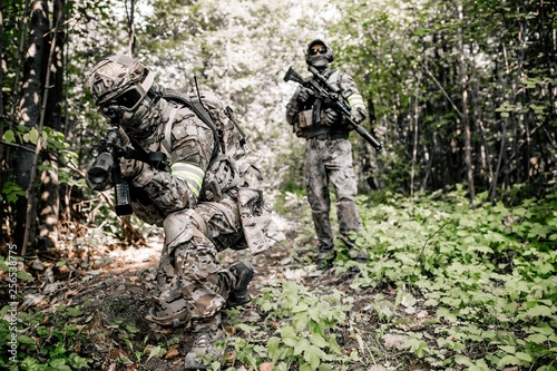 Armed soldiers in camouflage with sniper rifles walking along the path in the dense forest preparing for the assault. Military concept of disguised military