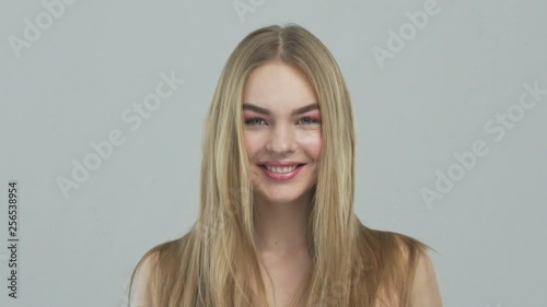 Beautiful blond woman with long hair. Portrait of young smiling woman with straight hair, posing at studio. Slow motion. Closeup face of caucasian model with stylish makeup. 