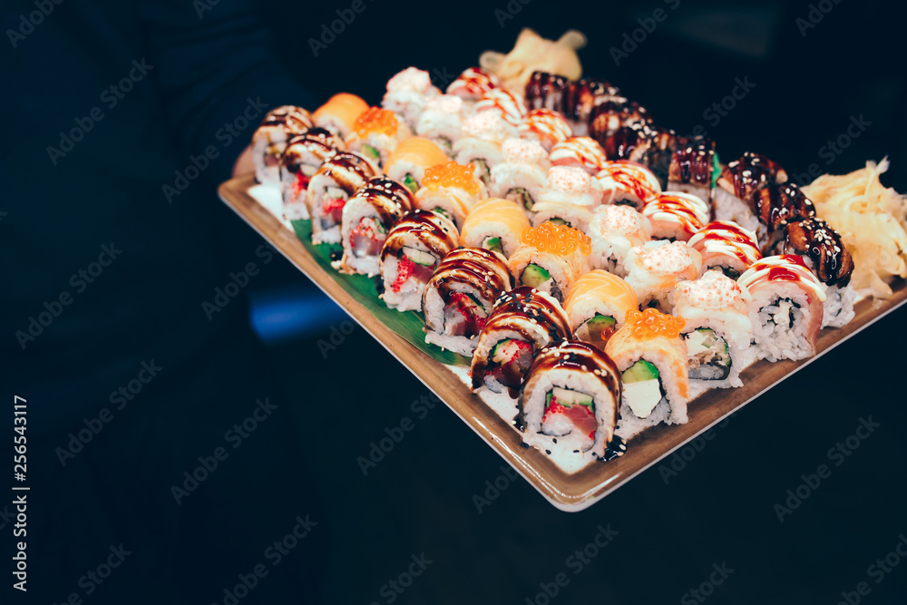 Close-up waiter holding Set of sushi red greed dragon, tuna Hokkaido  California Tobico philadelphia roll buffet in night dining restaurant.  Delicious served in a bar. The norwegian eel salmon Fish. Photos |