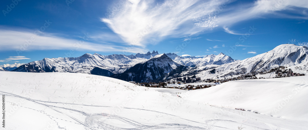 Panoramic landscape with mountain peaks in the French Alps, above La Toussuire village, on a sunny Winter day, in Les Sybelles ski area.