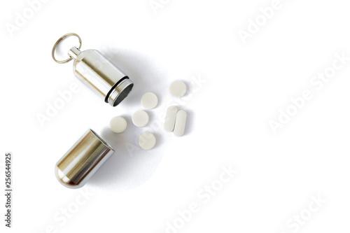 Silver medicine bottle with white pills next to it, isolated on white background. Portable key chain container for pills and small items, useful for hiking, camping, and expeditions.