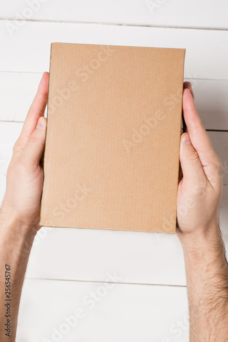 Rectangular box in male hands. Top view. White table on the background © somemeans