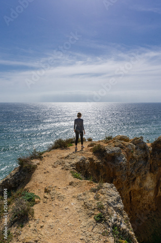 Woman hikes ocean ridge to horizon in Portugal