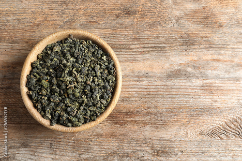 Bowl of Tie Guan Yin oolong tea leaves on wooden background, top view with space for text