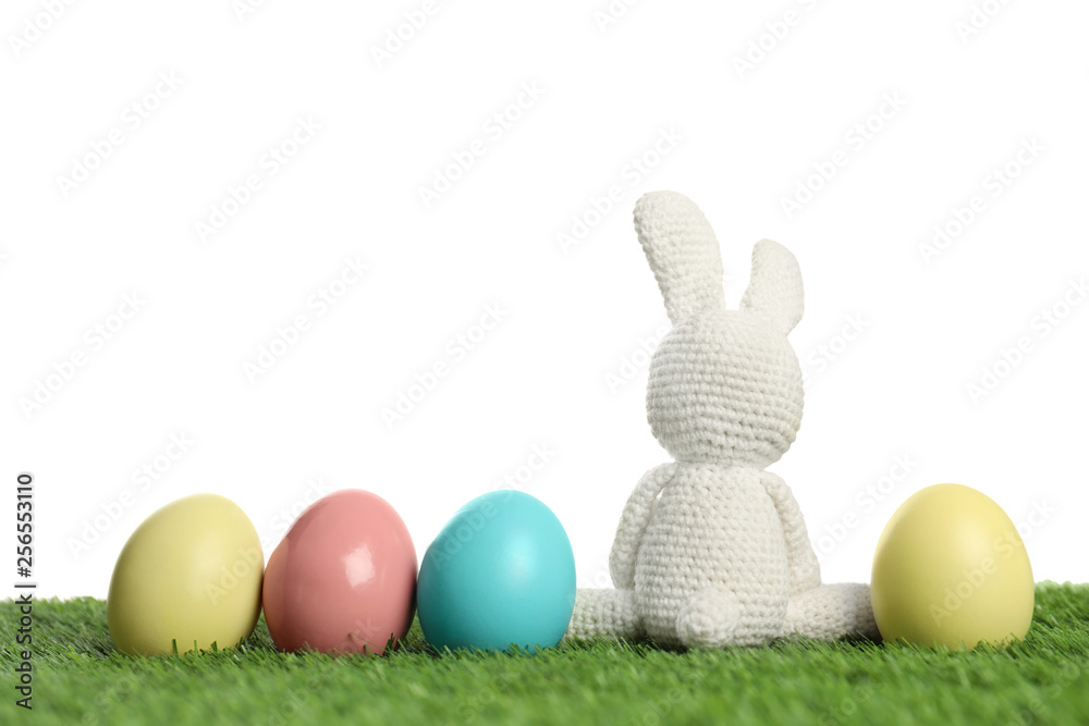 Cute Easter bunny toy and dyed eggs on green grass against white background, space for text