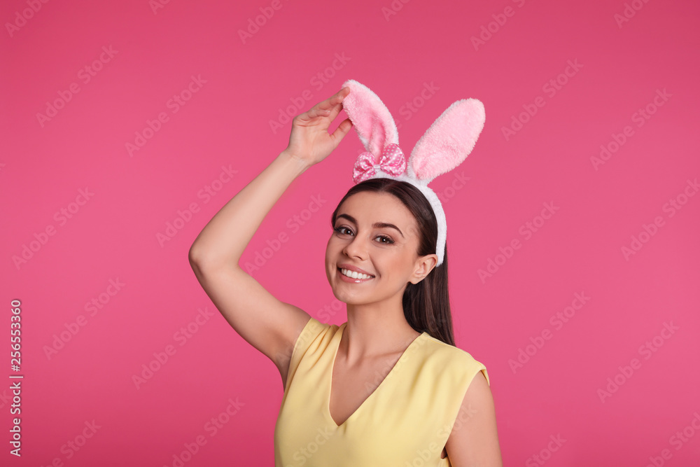 Portrait of beautiful woman in Easter bunny ears headband on color background