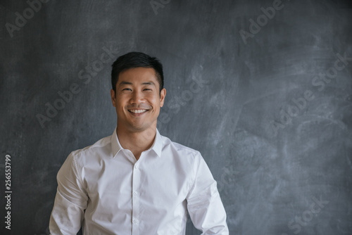 Smiling Asian businessman standing in front of a blank chalkboard