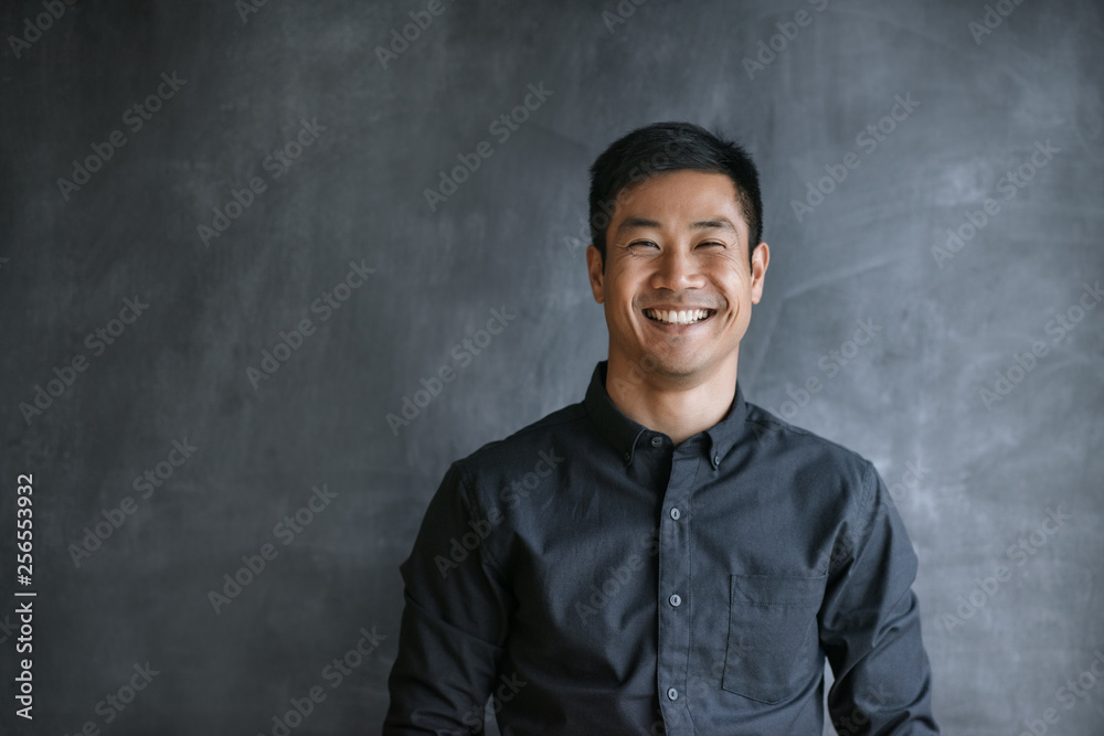 Smiling Asian businessman standing by a blank office chalkboard Smiling Asian businessman standing by a blank office chalkboard