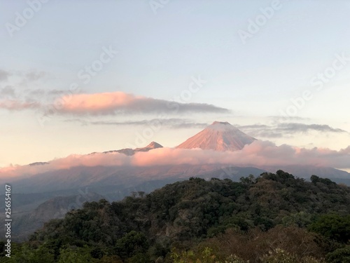 Grandioser Ausblick auf den massiven, aktiven Vulkan von Colima in Mexico mit ein paar Wolken am Himmel während die Sonne untergeht