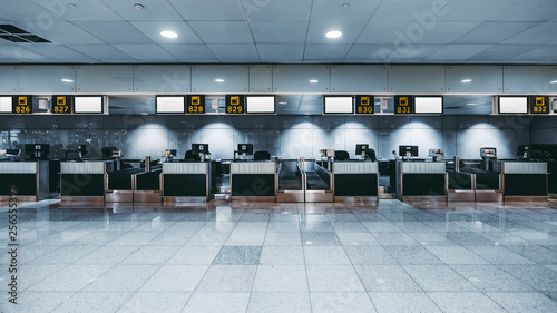 Front view of a check-in area in a modern airport: luggage accept terminals with baggage handling belt conveyor systems, multiple empty white informational LCD screen mockups, indexed check-in desks