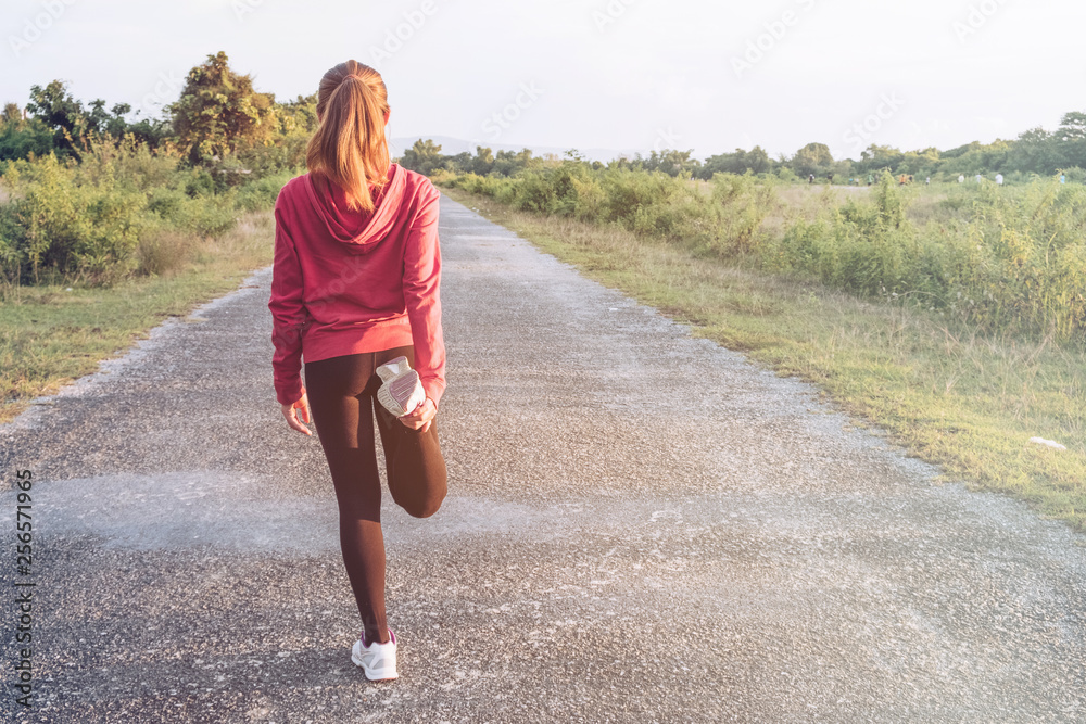 Shot of young fitness woman stretching legs before run on the long road. Woman warming up in the evening. Sport and Healthy concept. 