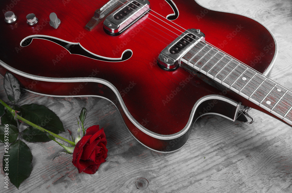 Obraz premium Electric guitar and red rose on a wooden table