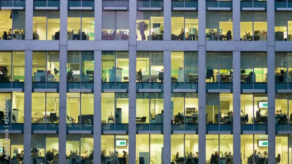 The exterior of an office block at night revealing the daily activity of office workers night themes of routines working late deadlines