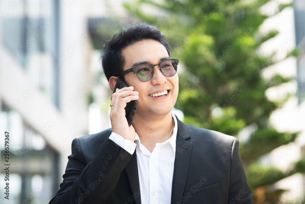 Handsome Asian businessman taking with phone outdoor.