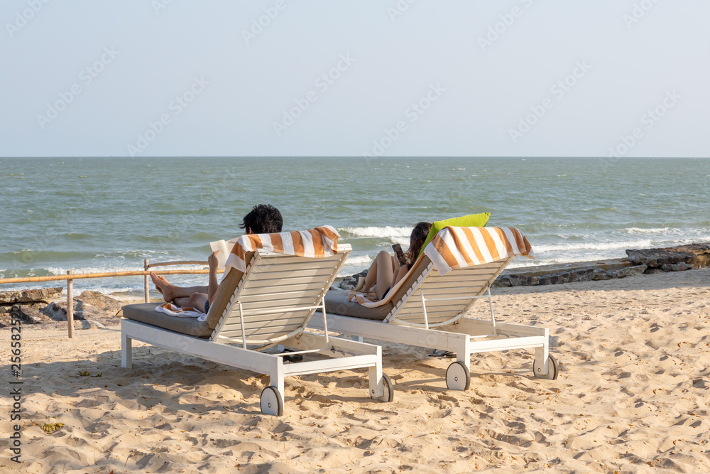 Young couple relaxing on the beach chair reading book and using cell phone.