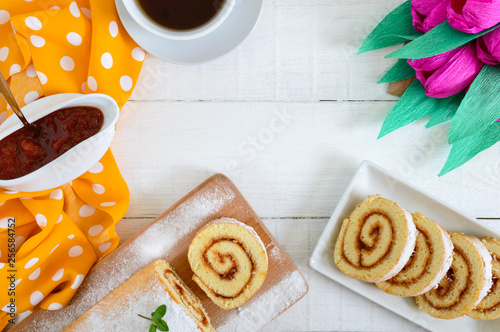 Delicious biscuit roll with apricot jam and a cup of tea on a white wooden table. Dessert for breakfast. Top view. Copy space photo