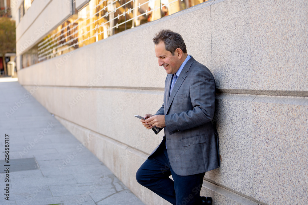 Middle aged handsome businessman using mobile phone app sending message outside office in urban city