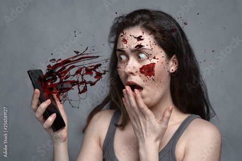 The concept of insecurity, spam, social problems,violence .With mobile phone flying blood splatter in the face, surprised, frightened girl. photo