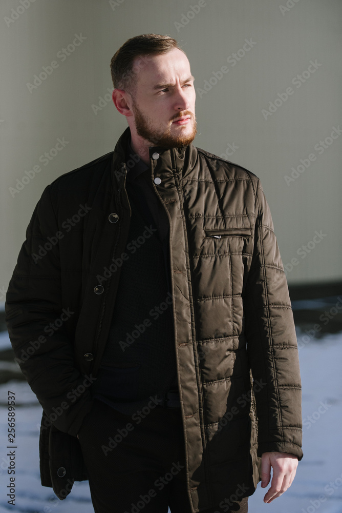 A man with a beard in a warm winter brown jacket poses for advertising of men's clothing in the winter. Advertising of men's clothing A man with a beard in a warm winter brown jacket poses for advertising of men's clothing in the winter. Advertising of men's clothing