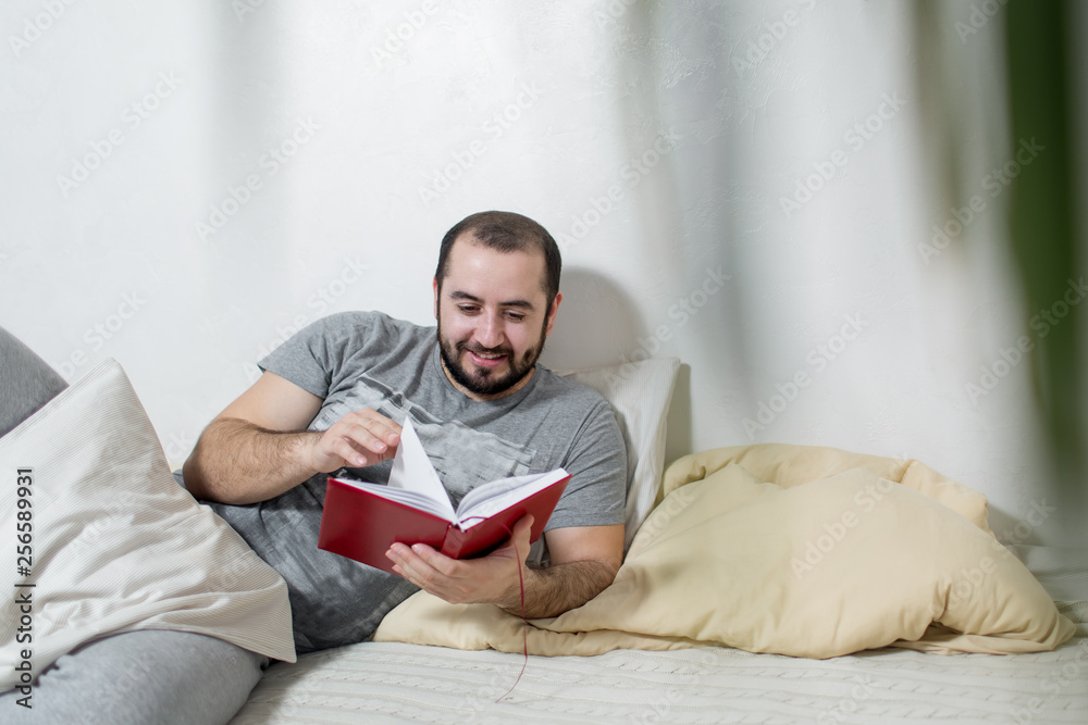 Young happy man reads the book in the bedroom. White background.