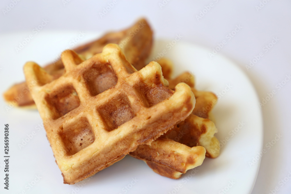 Belgian waffles in white plate. Healthy breakfast close up, pieces of freshly baked classic wafer Belgian waffles in white plate. Healthy breakfast close up, pieces of freshly baked classic wafer