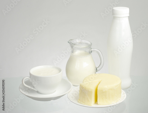 A cup of milk, a jug of milk, a bottle of milk and a piece of cheese on a white background.