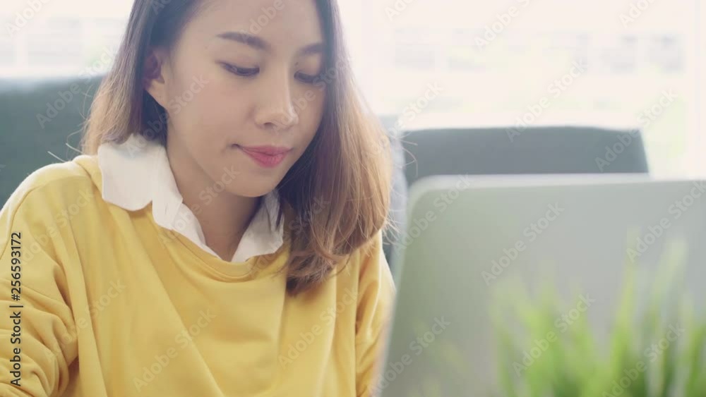 Beautiful young smiling asian woman working laptop on desk in living room at home. Asia business woman writing notebook document finance and calculator in home office. Enjoying time at home concept. Beautiful young smiling asian woman working laptop on desk in living room at home. Asia business woman writing notebook document finance and calculator in home office. Enjoying time at home concept.