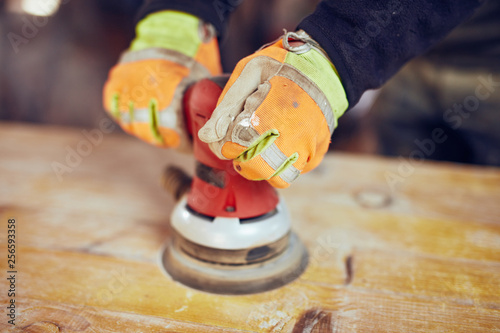 Male carpenter using orbital electric sander in a retro vintage workshop.